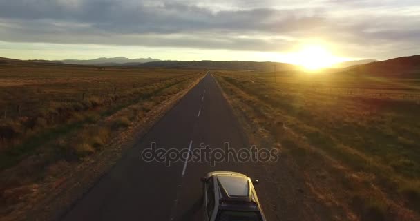 Aerial drone scene at sunset golden hour of route in steppe and van appears moving forward also man in bike. Mountains on the background. Camera flying over road. Desert rural landscape, Patagonia. — Stock Video