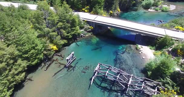 Luchtfoto drone scène van oude gebroken houten brug en de nieuwe snelweg over transparante, turkoois, cristal duidelijk (rivier), zijrivier van lake Correntoso, Patagonië. Camera panning omhoog. — Stockvideo