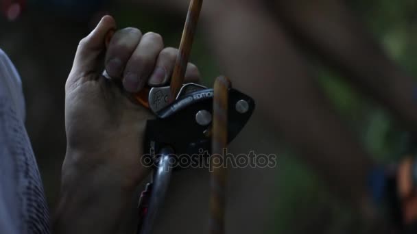 Klimmer belay met een grigri en een karabijnhaak. Detail van zijn handen en het touw passeren de grigri terwijl klimmer komt neer op de achtergrond als het doen van rappel. Slowmotion, 120 fps. — Stockvideo