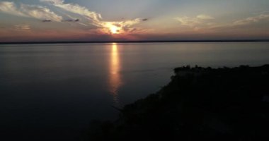 Sahilde uçan insansız hava aracı sahnesi ve gün batımında bitki örtüsünün silüeti, altın saat. Dalgalı renkli hareket. Turuncu, sarı güneş ufukta. Uruguay nehri, Caas, Rio Negro.