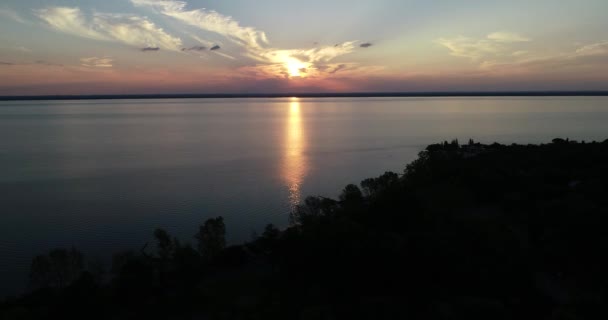 Flygdrönare scen flyger över stranden och sillhouete av vegetation vid solnedgången, gyllene timme. Rippel färgad rörelse. Orange, gul sol vid horisonten. Uruguayfloden, Caas, Rio Negro. — Stockvideo