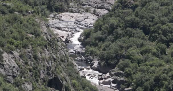 Mountain river with falls in eroded old rocky basin with woods and pedestrian bridge. Quebrada del Condorito National Park, Cordoba, Argentina — Stockvideo