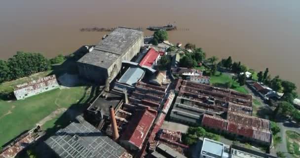 Ogólny widok z lotu ptaka na opuszczone szopy przemysłowe nad rzeką Urugwaj. Lecąc nad zardzewiałymi konstrukcjami w kierunku brązowej rzeki. Anglo, Unesco, Fray Bentos, Urugwaj — Wideo stockowe