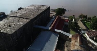 Eski terk edilmiş sanayi kulübelerinin ve Uruguay nehrindeki kırık rıhtımın havacılık genel manzarası. Paslı binaların üzerinden kahverengi nehre doğru uçuyor. Anglo, Unesco, Keşiş Bentos, Uruguay