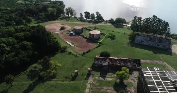 Letecká letecká scéna létající ze zrezivělých průmyslových přístřešků nad starými silami směrem k zelenému břehu. Unesco, Fray Bentos, Uruguay — Stock video