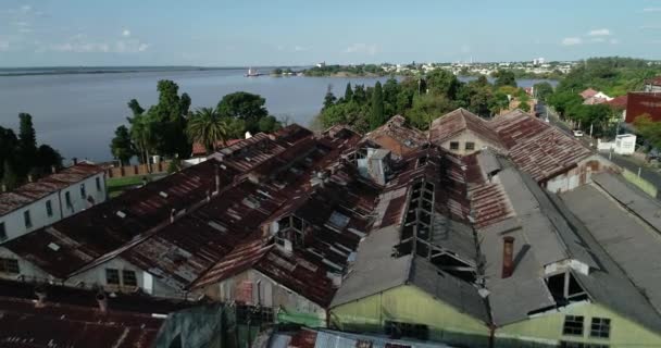 在生锈的、破碎的工业建筑金属屋顶上方的上空飞行。 城市和河流弯曲的背景。 Unesco, Anglo, Fray Bentos,乌拉圭 — 图库视频影像