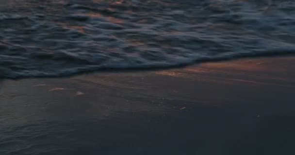Zbliżają się fale rozbijające się na piaszczystym brzegu o złotej godzinie. Szczegóły ruchu wody, pianki i odbicia pomarańczy na mokrym piasku. Tekstury i kolory wybrzeża o świcie. Urugwaj, Fray Bentos. — Wideo stockowe