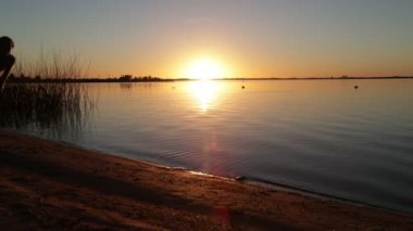Anne ve oğlunun kumlu bir sahilde sarılmak için koşması. Gün batımında sahilde mutlu bir aile. İnsan silueti, güneş ufukta. Villa Soriano, Uruguay