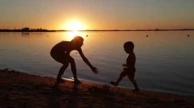 Oğlunun kumsalda annesine sarılmak için koşması, Silhouette of people. Gün batımında sahilde mutlu bir aile. Güneş ufukta görünüyor. Villa Soriano, Uruguay