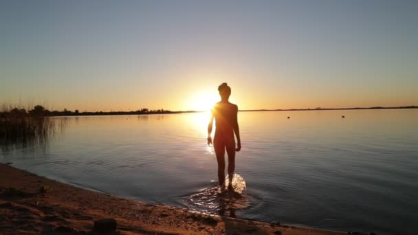 年轻女子在海滩、黄金时段、日落时慢吞吞地走在水里。 夫人的沉默在它的假日。 Villa Soriano，乌拉圭 — 图库视频影像