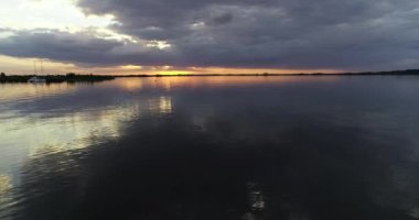 Küçük balıkçı teknesi gün batımında denize açılacak. Tekne sağdan çekiliyor. Arkasında turuncu renkler olan geniş, koyu renkli Rio Negro Nehri. Villa Soriano, Uruguay