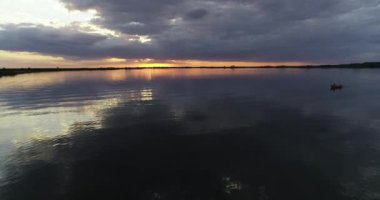 Küçük balıkçı teknesi gün batımında denize açılacak. Tekne sağdan çekiliyor. Arkasında turuncu renkler olan geniş, koyu renkli Rio Negro Nehri. Villa Soriano, Uruguay