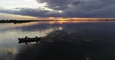 Gün batımında küçük bir balıkçı teknesini takip eden hava aracı. Arka planda bulutlar ve turuncu ufuk. Villa Soriano, Rio Negro, Uruguay.