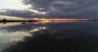 Gün batımında suyun üzerinde uçan bir hava sahnesi. Güneş ve turuncu renkler ufukta belirdi. Olay yerinden geçen küçük teknenin silueti. Villa Soriano, Rio Negro, Uruguay