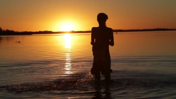 Anne ve oğlunun suda oynaması, dönmesi, uçması yavaş bir harekettir. Mutlu aile gün batımında tatilde. İnsan silueti, güneş ufukta. Villa Soriano, Uruguay — Stok video