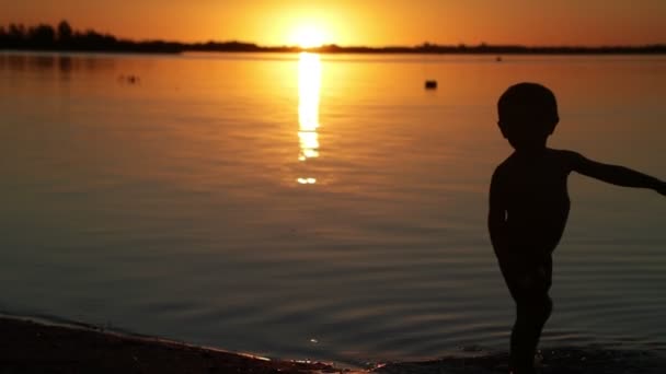A gyermek sziluettjének lassú mozgása a folyóban lévő vízben. Narancssárga nap rejtőzik a háttérben. Napnyugta. Soriano Villa, Uruguay megye — Stock videók