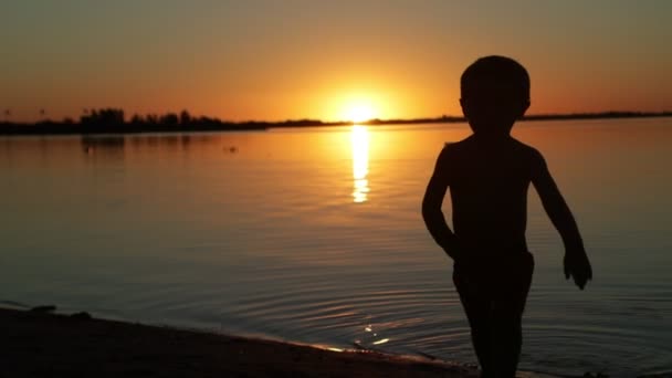 Повільний рух щасливої дитини йде з води до камери на заході сонця. Сонце ховається на горизонті, чорний силует людини, золота година. Вілла Соріано, Уругвай — стокове відео