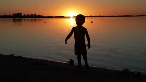 Lassú mozgás boldog gyermek sétál ki a vízből felé homokos strand naplementekor. A nap a horizonton rejtőzik, az ember fekete sziluettje, az arany óra. Soriano Villa, Uruguay megye — Stock videók