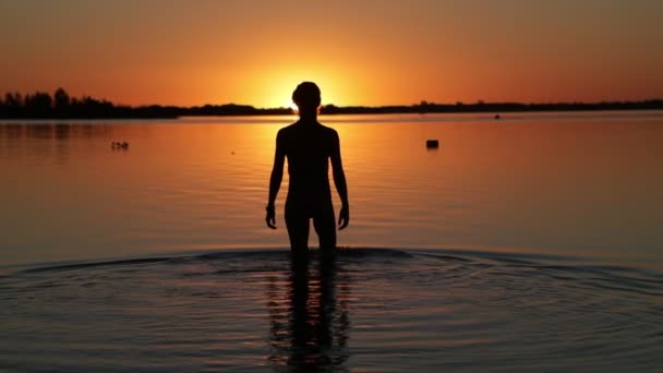 Movimento lento de silhueta ao pôr-do-sol da senhora entrando na água na praia. Cena preta e laranja. Villa Soriano, Uruguai . — Vídeo de Stock