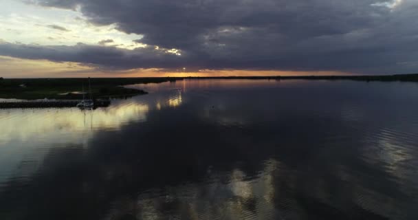 Aerial drone scene of orange sunset at wide natural river. Ascending to general view of long wooden dock with moored sailboats and green landscape. Villa Soriano, Rio Negro, Uruguay — Stock Video