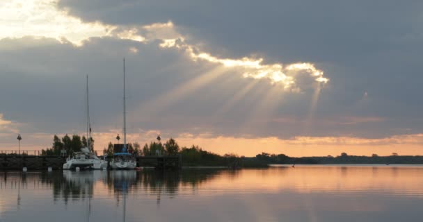 Barche a vela ormeggiate al molo di legno al tramonto. Riflessioni arancioni sull'acqua. Atmosfera tranquilla. Movimento tranquillo di acqua, ambiente verde naturale sullo sfondo. Villa Soriano, Uruguay — Video Stock