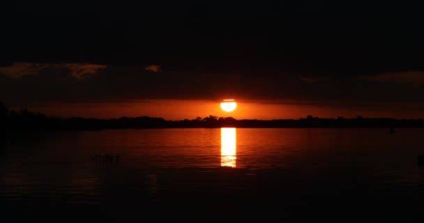 Natuurlandschap bij zonsondergang. Zon reflectie over het wateroppervlak terwijl het verschijnt van achteren van een wolk. Beweging van waterstroom met kleurrijke contrasterende reflecties van de lucht — Stockvideo