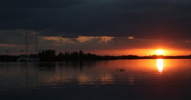 Hermoso atardecer en rio negro. Reflejos anaranjados y negros de sol y nubes a la derecha. Marine con veleros amarrados a la izquierda. Viaje, escena de vacaciones. Estilo de vida. Villa Soriano, Uruguay — Vídeo de stock