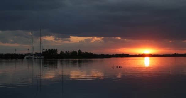 Belo pôr-do-sol no rio negro. Reflexos laranja e preto de sol e nuvens à direita. Fuzileiro naval com veleiros atracados à esquerda. Viagem, cena de férias. Estilo de vida. Villa Soriano, Uruguai — Vídeo de Stock