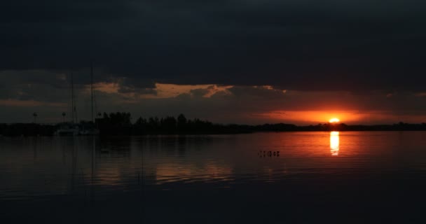Prachtige zonsondergang aan de Rio Negro rivier, zon verborgen aan de horizon. Oranje en zwarte reflecties van zon en wolken aan de rechterkant. Marinier met links afgemeerde zeilboten. Reizen, vakantie scene. Levensstijl — Stockvideo