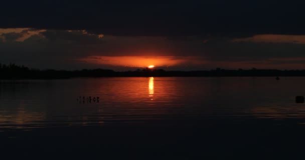 Zonsondergang aan de natuurlijke kust. Zon verstopt zich achter wolken aan de horizon. Oranje en zwart contrasterende kleuren reflecteren op het wateroppervlak. Waterstroming. Villa Soriano, Uruguay — Stockvideo