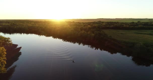 Gün batımında sakin nehirde kanoyla kürek çeken birini takip eden hava sahnesi. Fişekler ve turuncu yansımalar nehirde. Arka planda güneş ve yeşil doğal manzara. San Salvador nehri, Dolores, Uruguay — Stok video