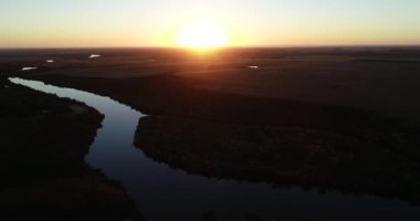 Gün batımında sakin nehrin yüksek panoramik manzarası. Doğal çevre, acımasız nehir. Turuncu gökyüzünün su yüzeyindeki yansıması. San Salvador nehri, Dolores şehri, Uruguay