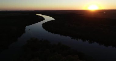 Gün batımında sakin nehrin havadan panoramik görüntüsü. Renkler farklı. Huzurlu su yüzeyinde yüzen teknenin siluetini takip ediyorum. Turuncu sahne. San Salvador nehri, Dolores şehri, Soriano, Uruguay