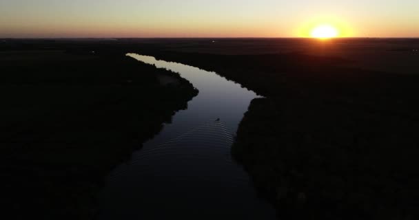 Vista panorámica aérea del río tranquilo al atardecer con barco navegando en una superficie tranquila. Colores contrastados, silueta naranja y negra de la naturaleza. Río San Salvador, ciudad de Dolores, Soriano, Uruguay — Vídeo de stock