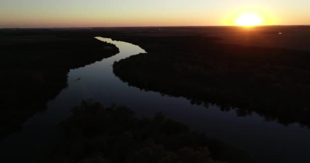 Повітряний панорамний вид спокійної ріки при заході сонця. Протилежні кольори. Слідом за силуетом човна, що пливе через спокійну поверхню води. Помаранчева дія. Річка Сан - Сальвадор, місто Долорес, Соріано, Уругвай — стокове відео