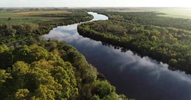 Aérea de río con vegetación natural a orillas del río y reflejo del cielo sobre la superficie del agua. Paisaje agrícola y puesta de sol al fondo. Dolores, Soriano, Uruguay — Vídeo de stock