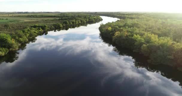 Aérea de río con vegetación natural a orillas del río y reflejo del cielo sobre la superficie del agua. Descubriendo el paisaje agrícola y la puesta de sol en el fondo. Dolores, Soriano, Uruguay — Vídeo de stock