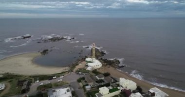 Turistik köyün üzerinden deniz fenerine doğru uçan bir hava sahnesi. Panoramik manzaradan, deniz feneri kulesinin yakınına kadar. Jose Ignacio, Maldonado, Uruguay