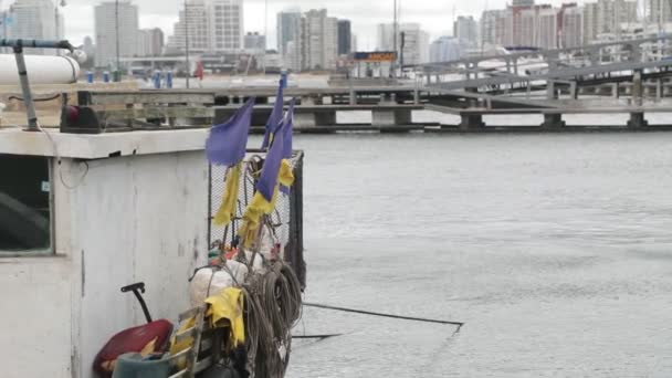 Lento acercamiento de cámara lateral del barco de pescadores. Banderas moviéndose con el viento. Muelle y paisaje urbano al fondo. Puerto de Punta del Este, Maldonado, Uruguay — Vídeo de stock