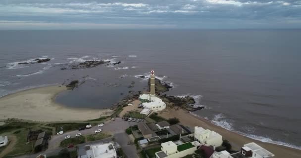Scène aérienne volant au-dessus du village touristique vers le phare. De la vue panoramique au gros plan senital de la tour du phare. Jose Ignacio, Maldonado, Uruguay — Video