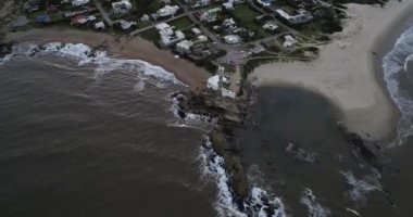 Kumlu sahildeki deniz fenerinin havadan çekilmiş görüntüsü. Günbatımında Pensinsula 'daki turistik kasabanın panoramik manzarasına geçiyoruz. Arka planda Jose Ignacio gölü var. Uruguay, Maldonado