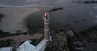 Fener odasının, kubbenin ve deniz fenerinin balkon güvertesinin havadan kapatılması. İnşaat alanında dönen insanlar, galeri güvertesinde yürüyen insanlar. Arka planda Rocky Coast var. Jose Ignacio Uruguay, Maldonado