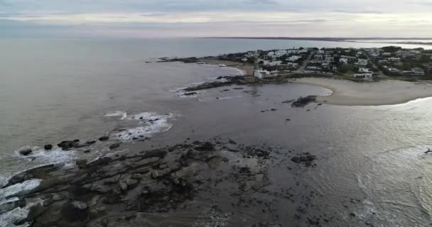 Scena aerea drone di paesaggio panoramico di penisola rocciosa con faro e villaggio turistico sullo sfondo. Scendendo sopra l'acqua e rocce. Jose Ignacio città, Maldonado, Uruguay — Video Stock