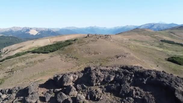 Vuelo aéreo sobre la cima de la montaña volcánica roja, pasando cerca de rocas y pastizales. Cadenas montañosas andinas al fondo. Cerro Colorado, San Martín de los Andes, Neuquén, Argentina — Vídeos de Stock