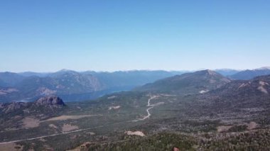 Göl ve dağ zincirinin geniş manzaralı insansız hava aracı manzarası kayalık dağ zirvesinde manzarayı seyreden genç bir adamı keşfediyor. Parallax. San Martin de los Andes, Neuquen, Arjantin