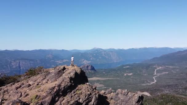 Scène aérienne de drone retournant le point d'intérêt sur le jeune homme athlétique au-dessus du sommet de la montagne en regardant un large paysage de lacs et de chaînes de montagnes. San Martin de los Andes, Neuquen, Argentine — Video