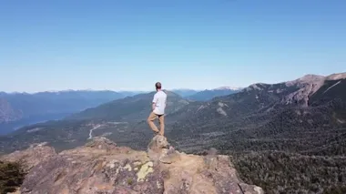Hava aracı sahnesi, dağ zirvesinde genç atletik bir adamın göller ve dağ zincirlerinin geniş manzarasını izleyerek ilgi odağı haline geliyor. San Martin de los Andes, Neuquen, Arjantin