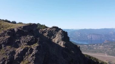 Kayalık Dağ Zirvesi 'nde, göllerin ve dağ zincirlerinin manzarasını izleyen genç bir adama doğru uçan hava aracı. Parallax. San Martin de los Andes, Neuquen, Arjantin