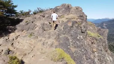 Uçan genç atletik adam kayalık zirveye ulaşıyor ve And Dağları Zinciri ve göllerin panoramik manzarasını keşfediyor. Parallax. Cerro Colorado yanardağına yolculuk, San Martin de los Andes, Neuquen
