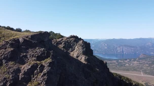 Kayalık Dağ Zirvesi 'nde, göllerin ve dağ zincirlerinin manzarasını izleyen genç bir adama doğru uçan hava aracı. Parallax. San Martin de los Andes, Neuquen, Arjantin — Stok video